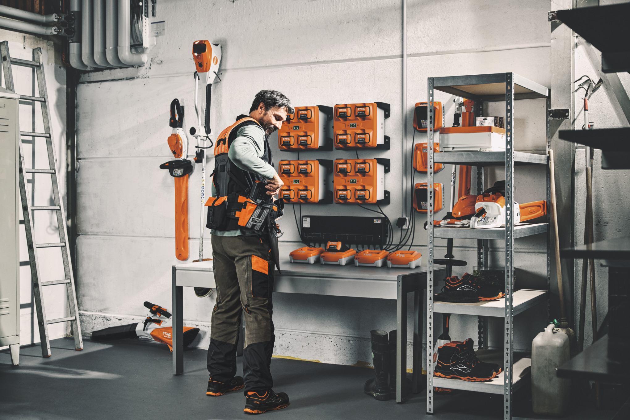 A man in a storage room with STIHL tools and batteries wears the STIHL ADVANCE X-Flex modular harness system 