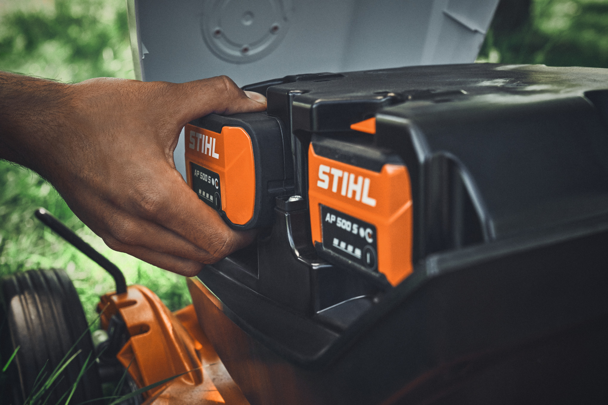 One person inserts a STIHL AP 500 S battery into a STIHL cordless lawn mower