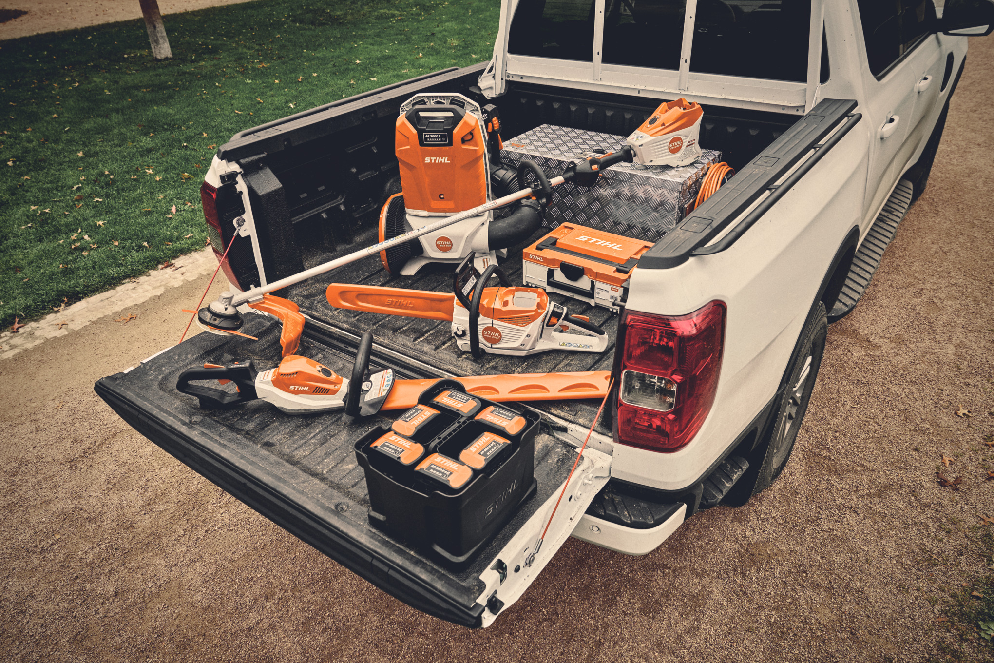 Various battery-powered tools from the STIHL AP system and the matching batteries on the loading area of a vehicle.