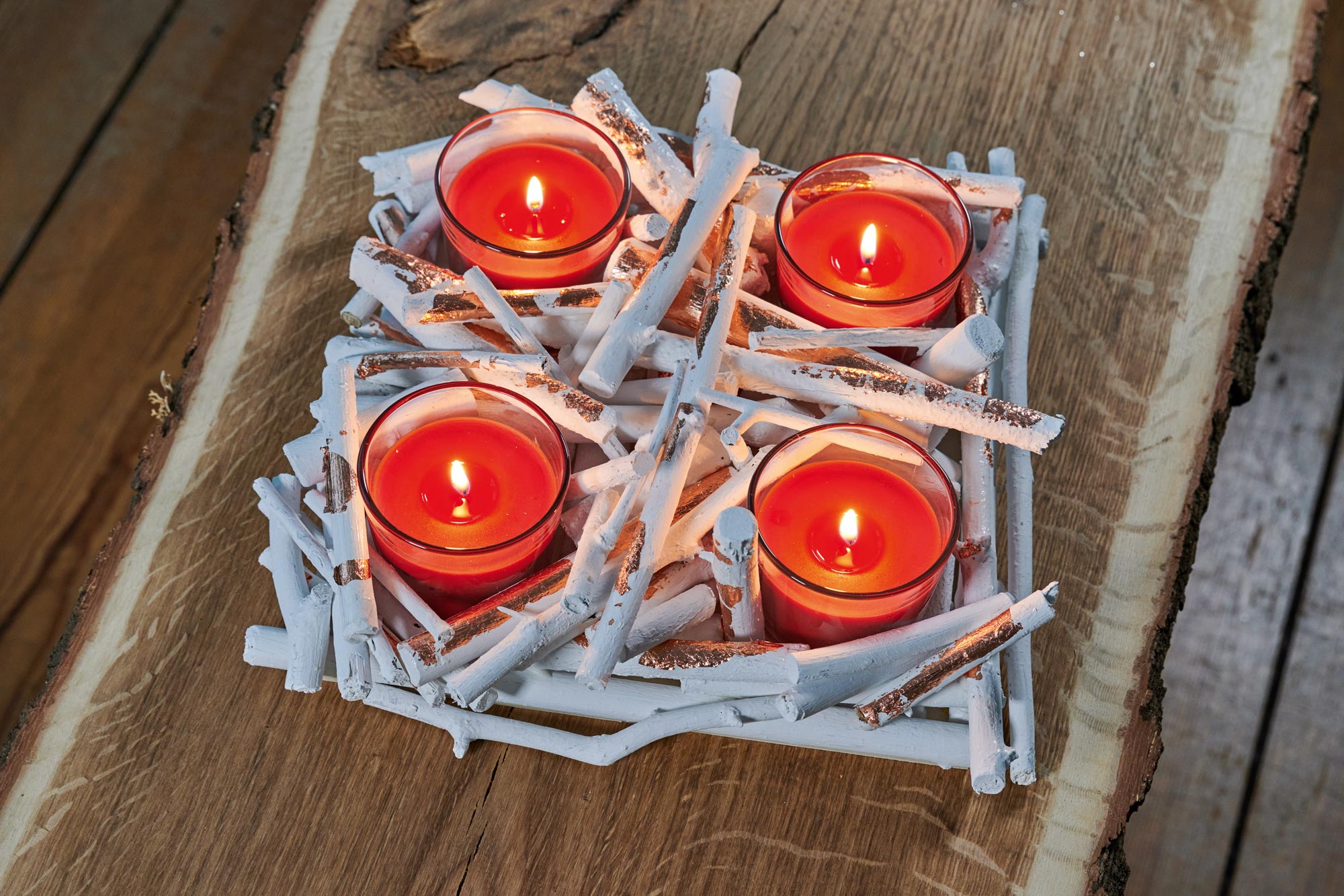 Four red candle glasses burning in a homemade twig advent wreath