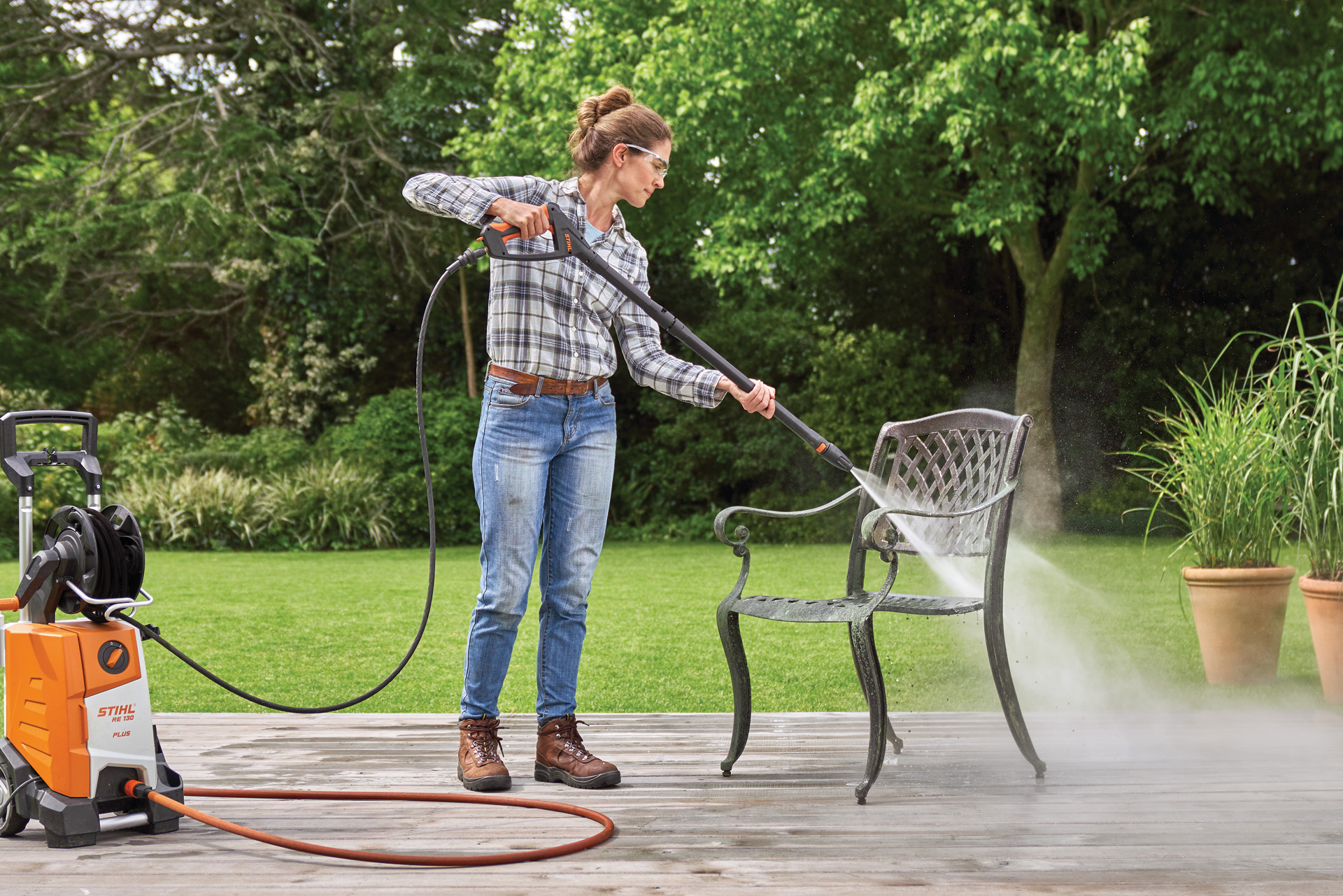 A woman using the STIHL RE 130 Plus high-pressure cleaner on a metal chair on a patio in a garden