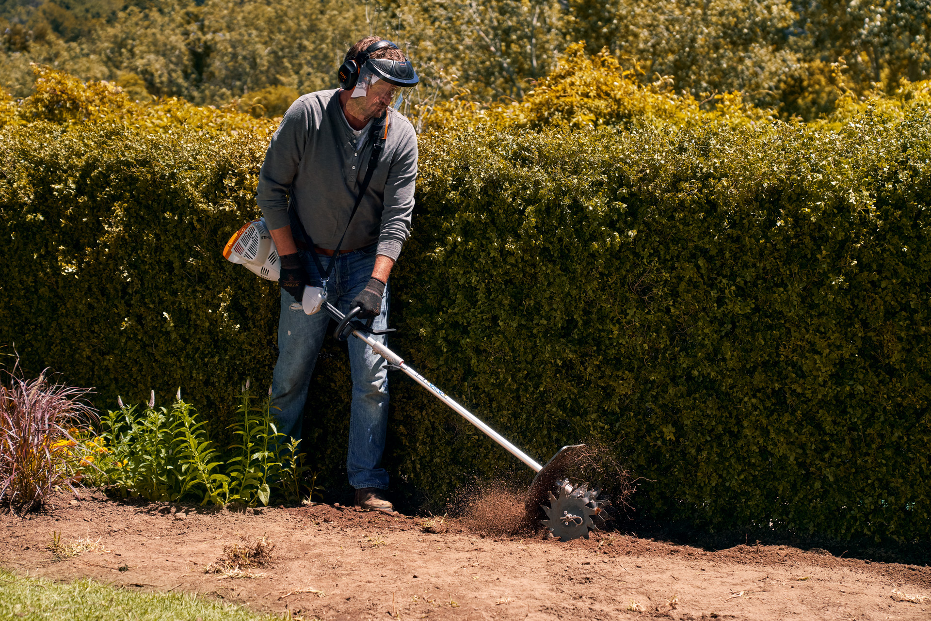 A man wearing a face visor and gloves using the STIHL KombiEngine KM 56 RC-E