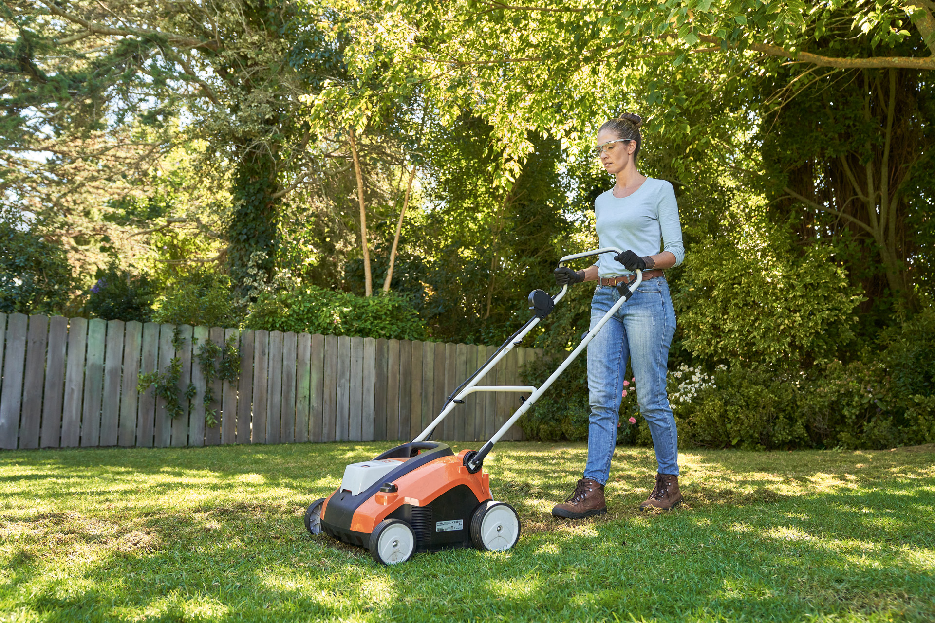 Woman aerating lawn with a STIHL RLA 240 cordless lawn scarifier in the garden, wearing safety glasses and work gloves.