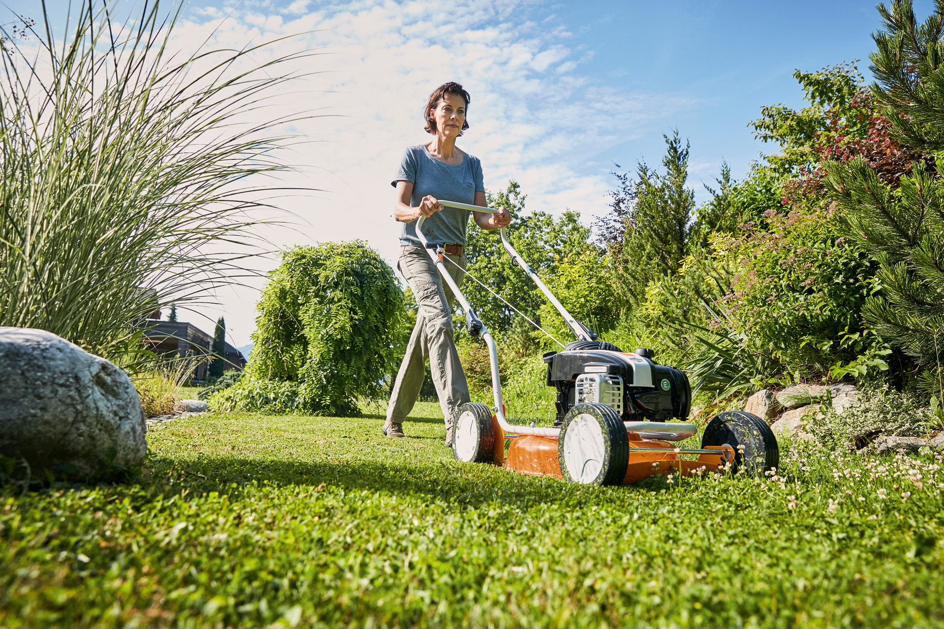 A woman using a STIHL RM 2 R petrol mulching lawn mower on a green area