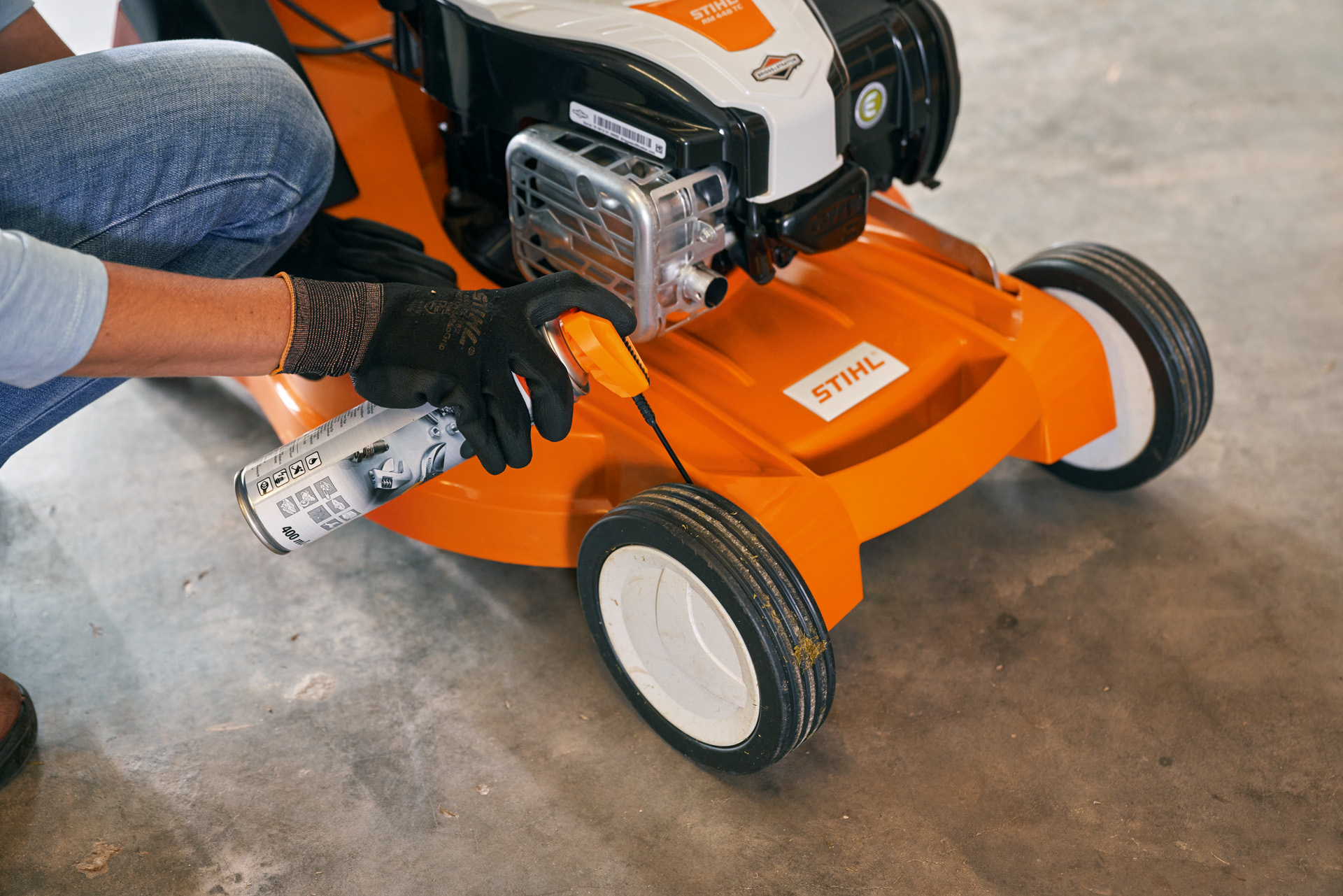 Woman storing her STIHL RM 448 TC petrol lawn mower in a garage 